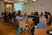 Abgebildet ist ein Raum, mit einer Workshop-Gruppe. Die Tische sind in Form eines Rechteckes angeordnet. Rundherum sitzen TeilnehmerInnen und hören dem Referenten, Fabian Reicher (Back Bone - Mobile Jugendarbeit) zu. Herr Reicher ist schwarz gekleidet. Hinter ihm an der Wand eine Powerpoint-Präsentation. Außerdem ist im Hintergrund eine geschlossene Glastüre zu sehen.